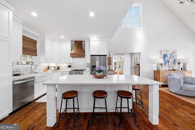 kitchen featuring sink, premium range hood, white cabinetry, appliances with stainless steel finishes, and a center island