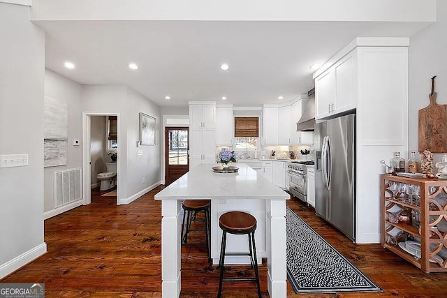 kitchen featuring a kitchen island, appliances with stainless steel finishes, white cabinetry, a breakfast bar area, and dark wood-type flooring