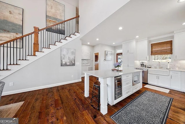 kitchen featuring a kitchen island, sink, white cabinets, beverage cooler, and dark wood-type flooring