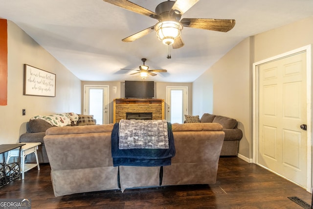 living room featuring a stone fireplace, visible vents, baseboards, vaulted ceiling, and dark wood-style floors