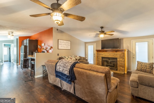 living area featuring dark wood-style floors, baseboards, vaulted ceiling, and a stone fireplace