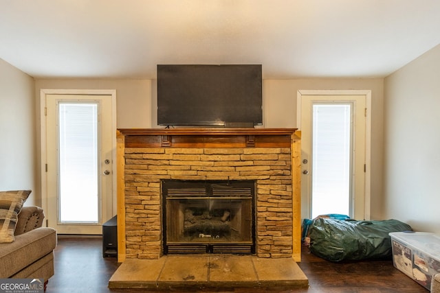 living room with a stone fireplace and dark wood-type flooring