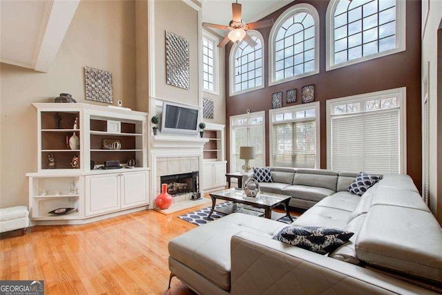 living room with hardwood / wood-style flooring, a tile fireplace, a towering ceiling, and ceiling fan