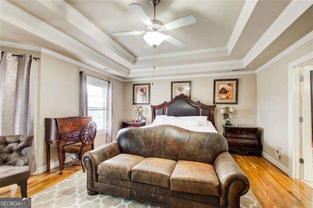 bedroom featuring ceiling fan, ornamental molding, a raised ceiling, and light wood-type flooring