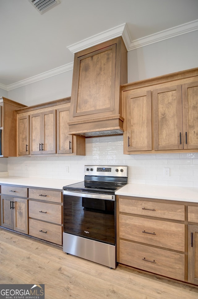 kitchen featuring premium range hood, stainless steel electric range oven, ornamental molding, light hardwood / wood-style floors, and backsplash
