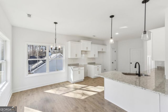 kitchen with sink, backsplash, light stone countertops, light hardwood / wood-style floors, and white cabinets