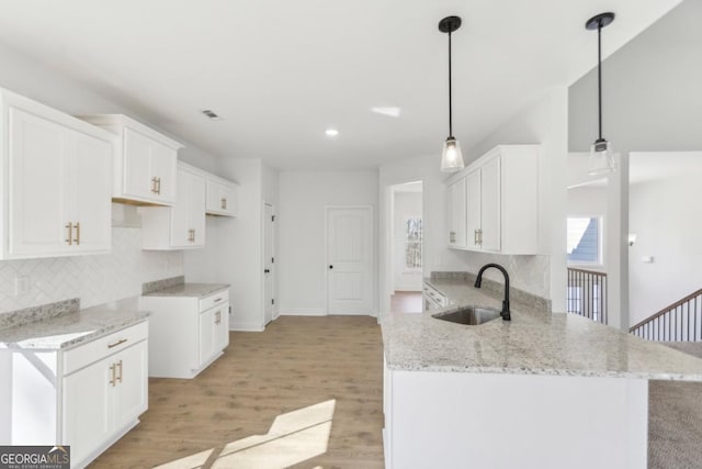 kitchen featuring sink, light hardwood / wood-style flooring, light stone countertops, white cabinets, and decorative light fixtures