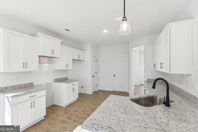 kitchen featuring pendant lighting, sink, white cabinetry, light stone counters, and light hardwood / wood-style floors