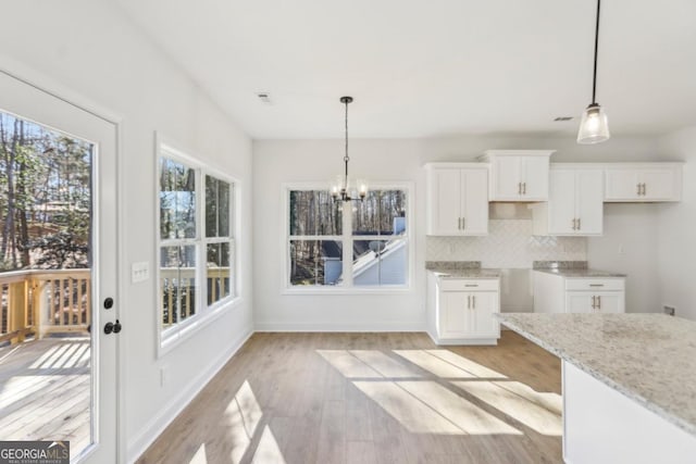 kitchen with white cabinetry, hanging light fixtures, light stone counters, light hardwood / wood-style floors, and decorative backsplash