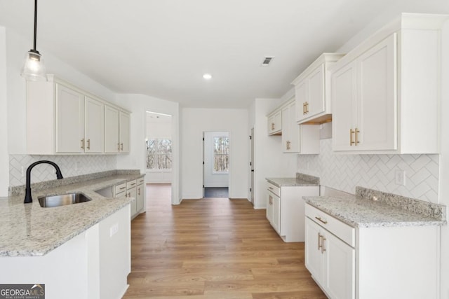 kitchen with sink, pendant lighting, white cabinets, and light stone counters