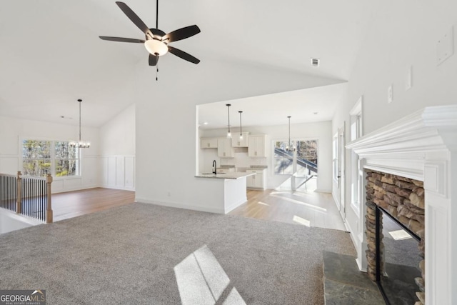 unfurnished living room with a stone fireplace, sink, a wealth of natural light, and high vaulted ceiling