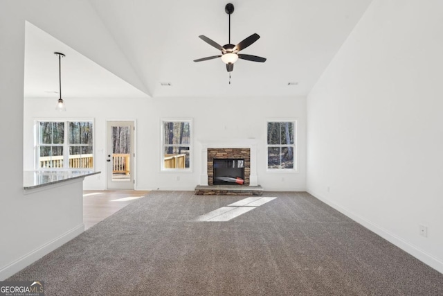 unfurnished living room with plenty of natural light, light colored carpet, and a stone fireplace