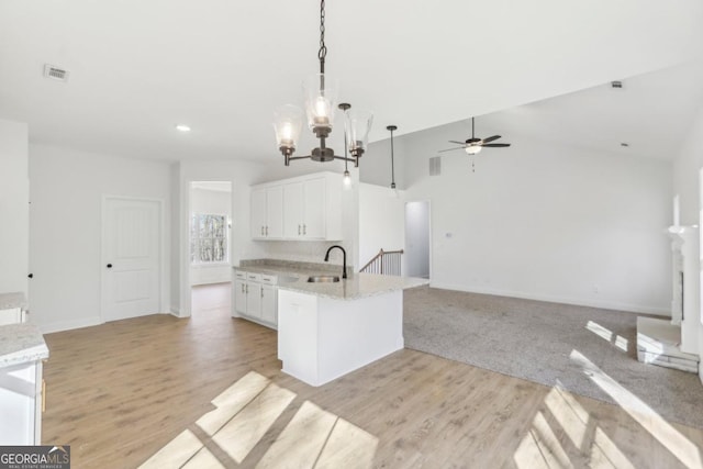 kitchen featuring decorative light fixtures, sink, white cabinets, light stone countertops, and light wood-type flooring