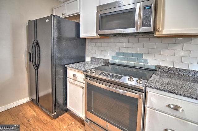 kitchen featuring appliances with stainless steel finishes, white cabinetry, dark stone countertops, light hardwood / wood-style floors, and decorative backsplash