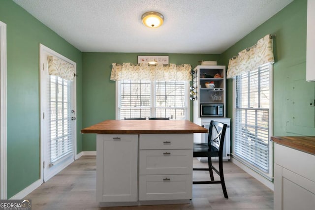 interior space featuring wood counters, a wealth of natural light, light hardwood / wood-style floors, and white cabinets