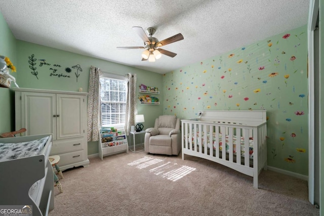 carpeted bedroom with ceiling fan, a crib, and a textured ceiling