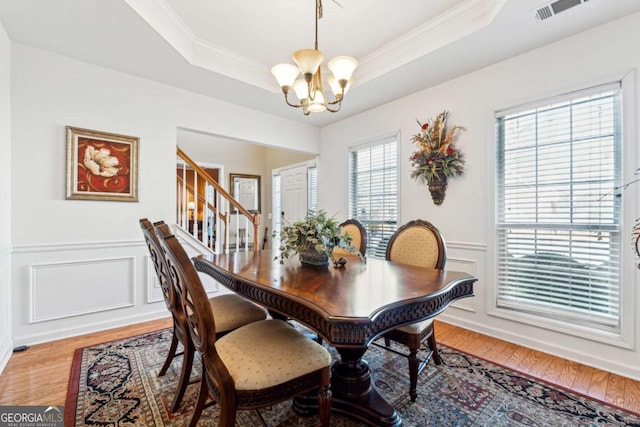 dining space featuring a raised ceiling, ornamental molding, a notable chandelier, and light wood-type flooring