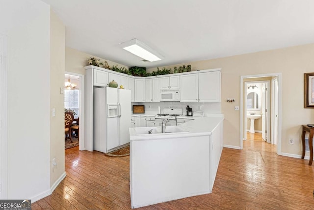 kitchen with sink, white cabinetry, kitchen peninsula, white appliances, and light hardwood / wood-style floors