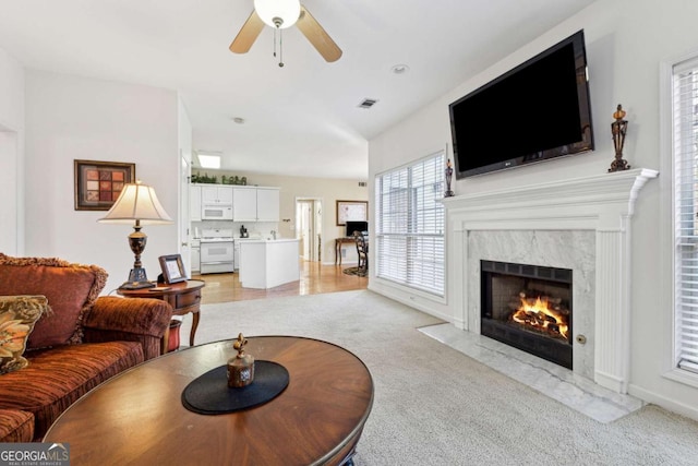 living room with ceiling fan, lofted ceiling, light colored carpet, and a high end fireplace