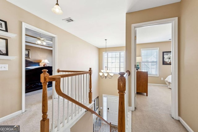 hallway with light carpet and an inviting chandelier