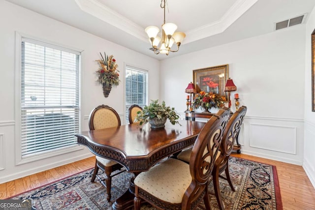 dining space with an inviting chandelier, a tray ceiling, hardwood / wood-style floors, and crown molding