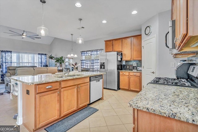 kitchen with decorative light fixtures, sink, light stone counters, stainless steel appliances, and a center island with sink