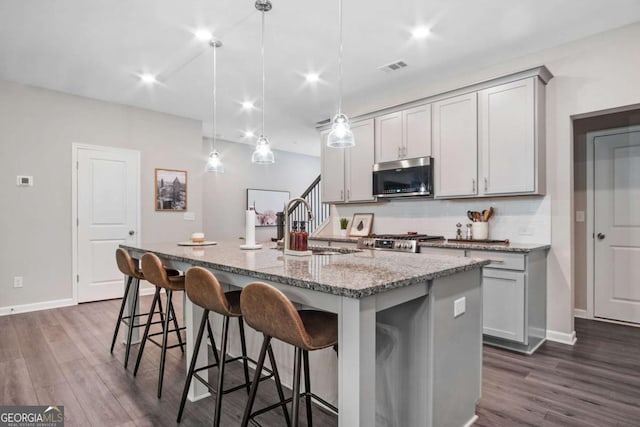 kitchen with tasteful backsplash, visible vents, light stone counters, stainless steel microwave, and a sink