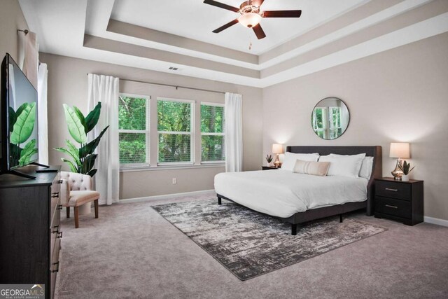 carpeted bedroom featuring baseboards, visible vents, a tray ceiling, and a ceiling fan