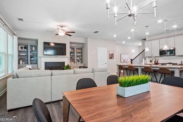 dining space with visible vents, a ceiling fan, dark wood-style floors, stairway, and a fireplace