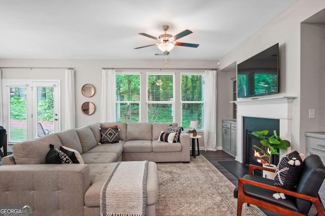 living room featuring ceiling fan, a glass covered fireplace, and dark wood finished floors