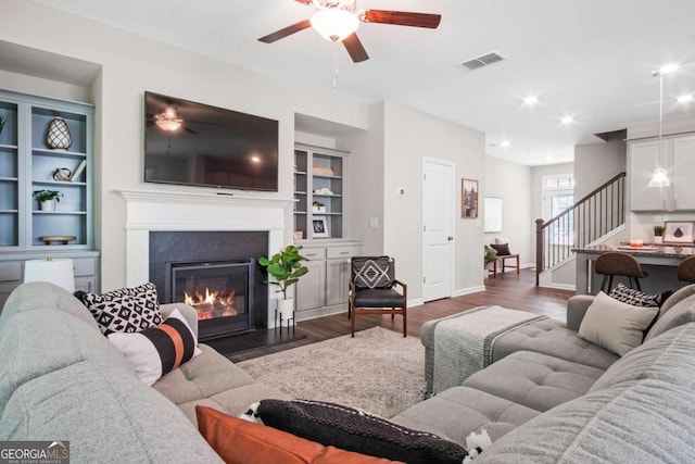 living area with visible vents, stairway, a glass covered fireplace, wood finished floors, and baseboards