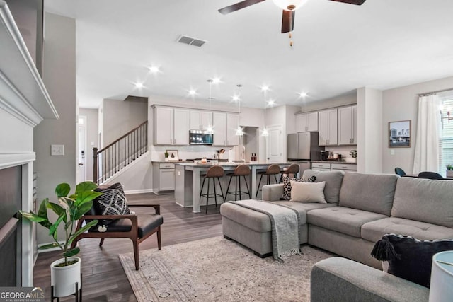 living room with ceiling fan, a fireplace, visible vents, stairway, and dark wood-style floors