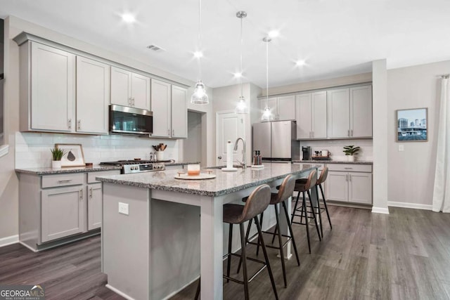 kitchen with dark wood finished floors, a breakfast bar area, appliances with stainless steel finishes, gray cabinets, and a sink