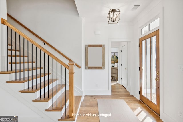 foyer with baseboards, visible vents, stairway, wood finished floors, and a chandelier