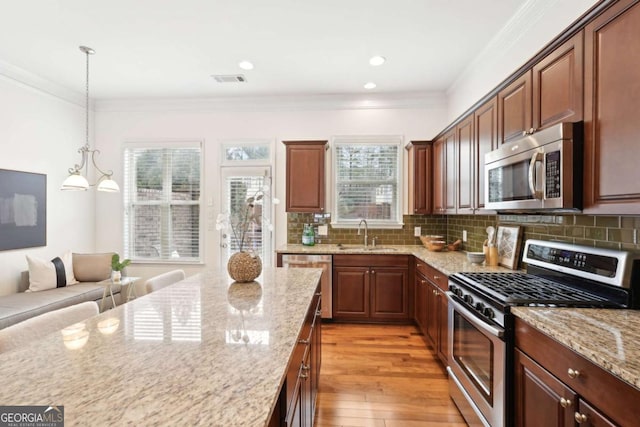 kitchen with sink, crown molding, pendant lighting, stainless steel appliances, and light stone countertops