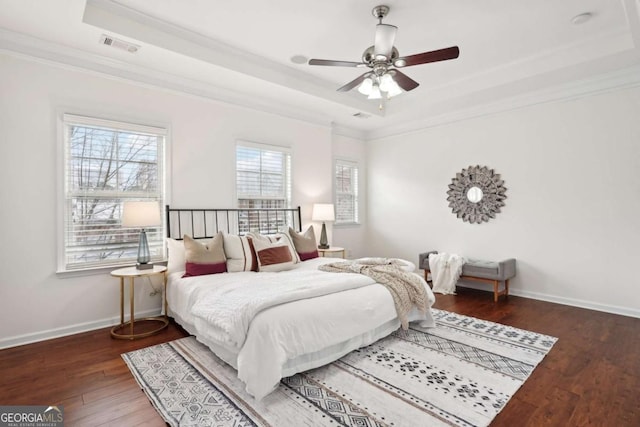 bedroom with a raised ceiling, crown molding, dark wood-type flooring, and ceiling fan