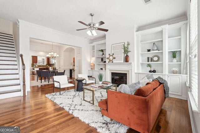 living room featuring a wealth of natural light, ceiling fan with notable chandelier, light hardwood / wood-style flooring, crown molding, and built in shelves