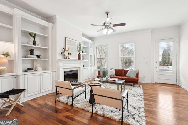 living room featuring crown molding, wood-type flooring, built in shelves, and ceiling fan