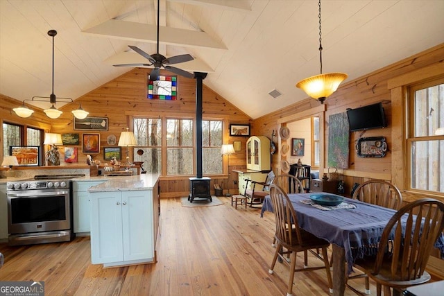 kitchen featuring hanging light fixtures, wooden walls, light stone counters, electric stove, and a wood stove