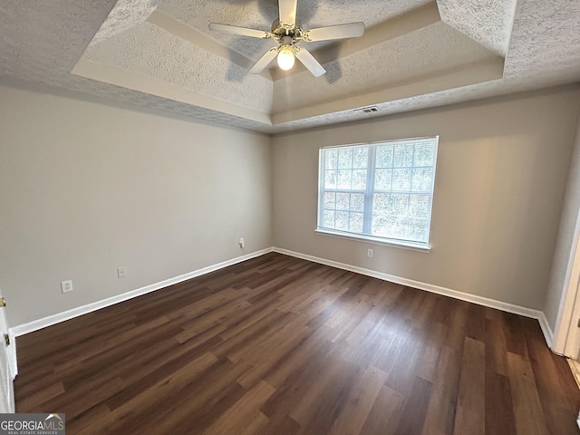 interior space with ceiling fan, dark wood-type flooring, a textured ceiling, and a tray ceiling