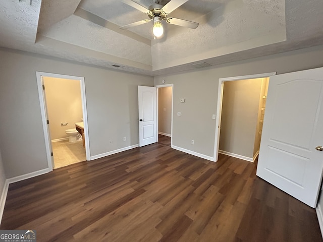 unfurnished bedroom with dark hardwood / wood-style floors, connected bathroom, a textured ceiling, and a tray ceiling