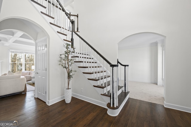 stairs with a high ceiling, coffered ceiling, wood finished floors, and baseboards