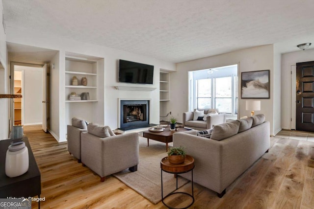 living room with built in features, a textured ceiling, and light wood-type flooring