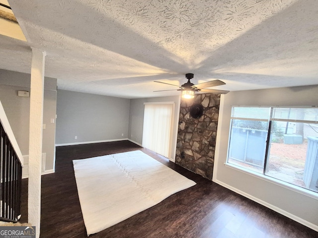 unfurnished living room featuring dark wood-type flooring, ceiling fan, and a textured ceiling