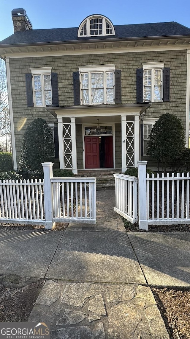 view of front of house featuring brick siding, a fenced front yard, and a chimney