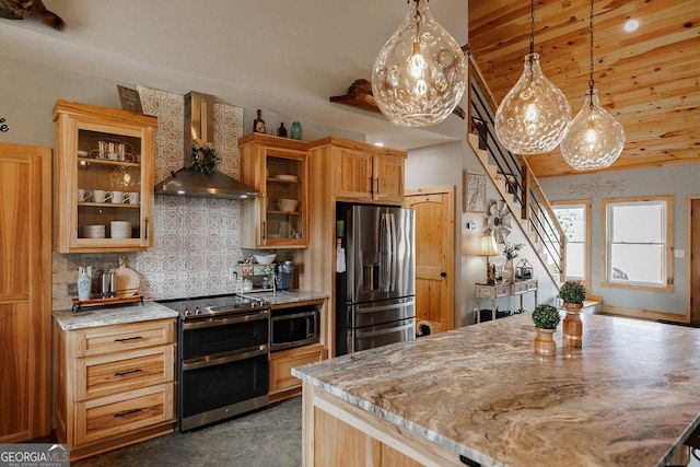 kitchen with stainless steel appliances, wall chimney range hood, light stone counters, and decorative light fixtures