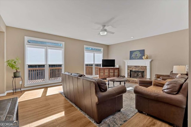 living room with ceiling fan, a stone fireplace, and light hardwood / wood-style floors