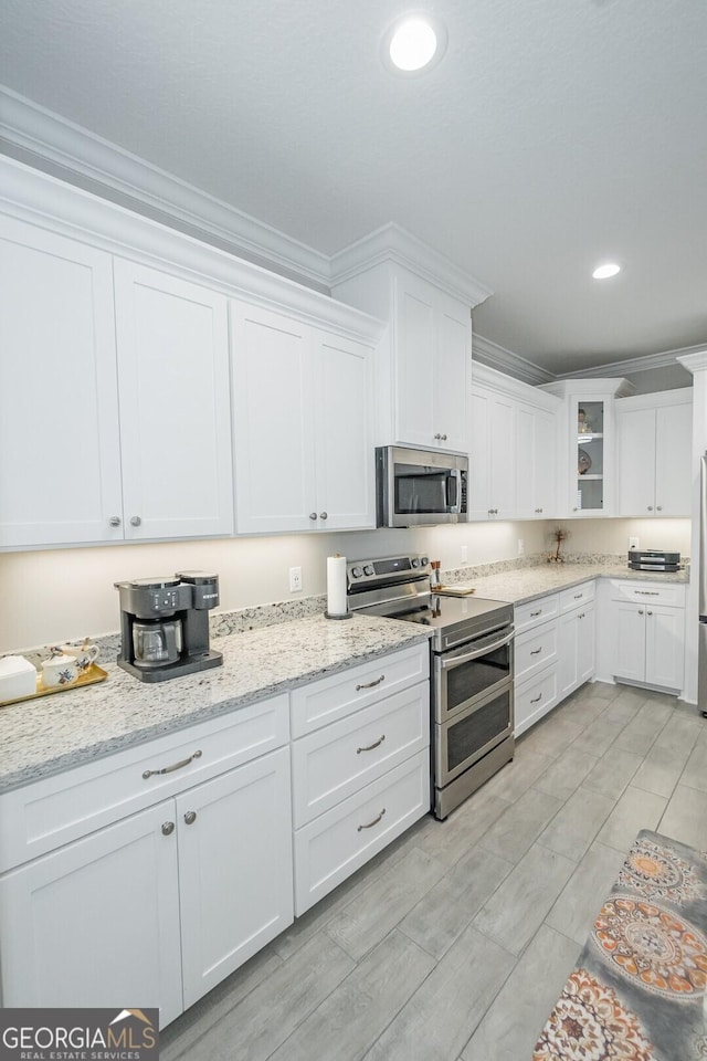 kitchen with crown molding, appliances with stainless steel finishes, light stone counters, and white cabinets