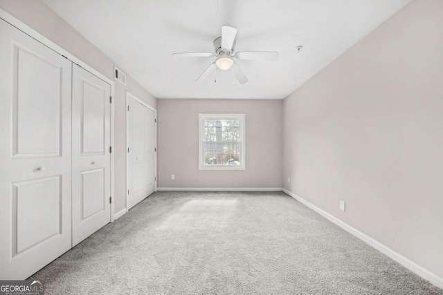 unfurnished bedroom with two closets, light carpet, and ceiling fan