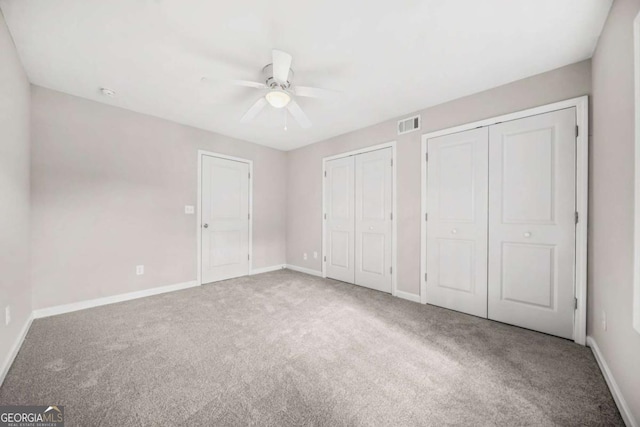 unfurnished bedroom featuring ceiling fan, carpet, and two closets